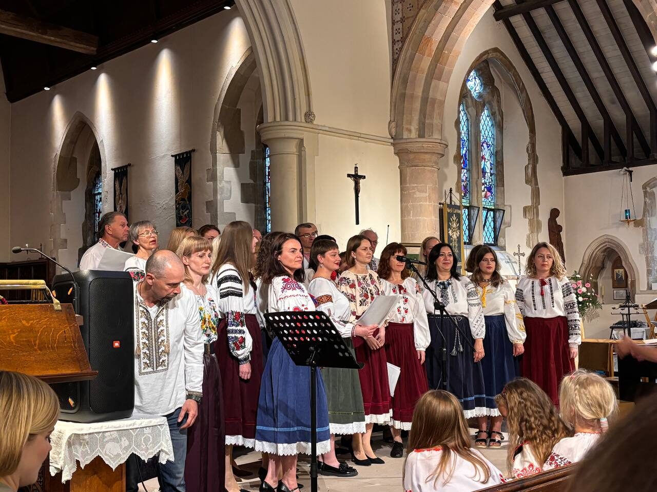 Ukrainian Voices choir singing together inside a church, conductor leading from the front.